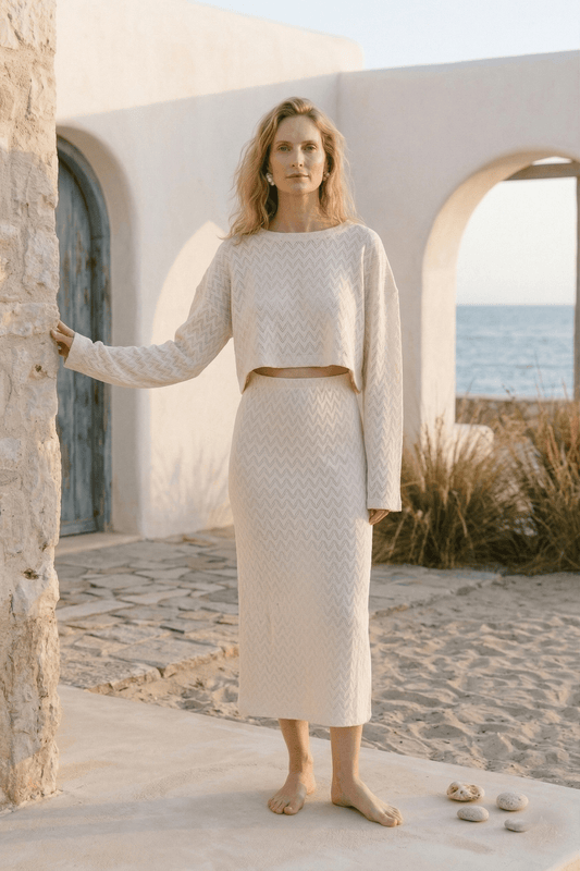 Model wearing a Crochet Organic Cotton Long Sleeve Top with matching skirt, set against a beachside backdrop.
