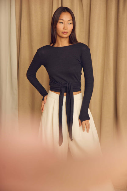Model wearing a Black Wool Wrap Top with thumb holes and a tied waist, styled with wide-legged pants.