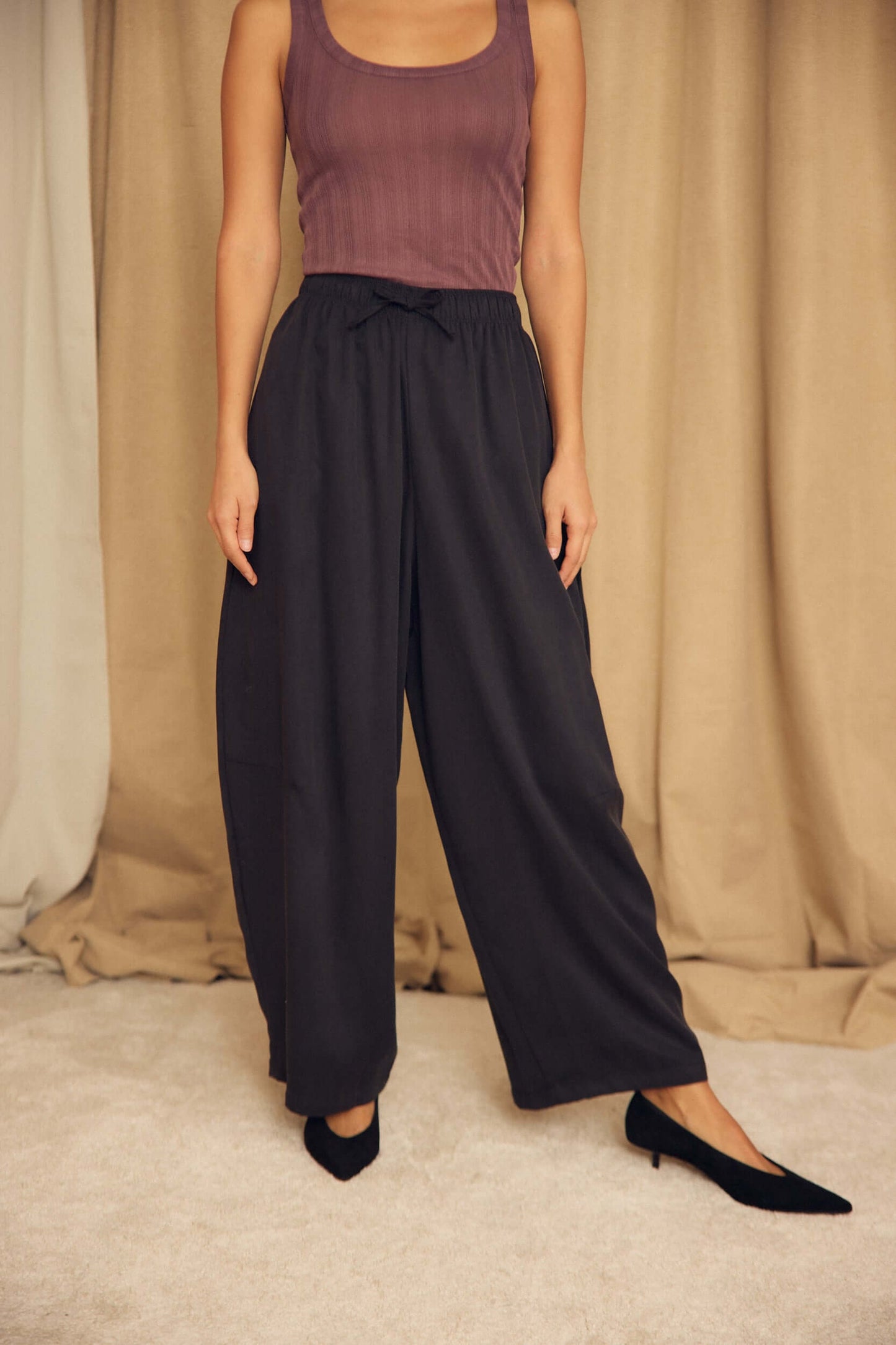 Model wearing Black Lyocell Barrel-Leg Trousers with a fitted top and heels, showcasing relaxed tailoring style.