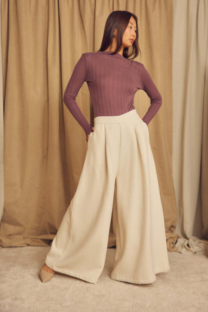 Woman wearing Ecru Organic Cotton Wide Trousers with a fitted long-sleeve top, posing against a neutral backdrop.
