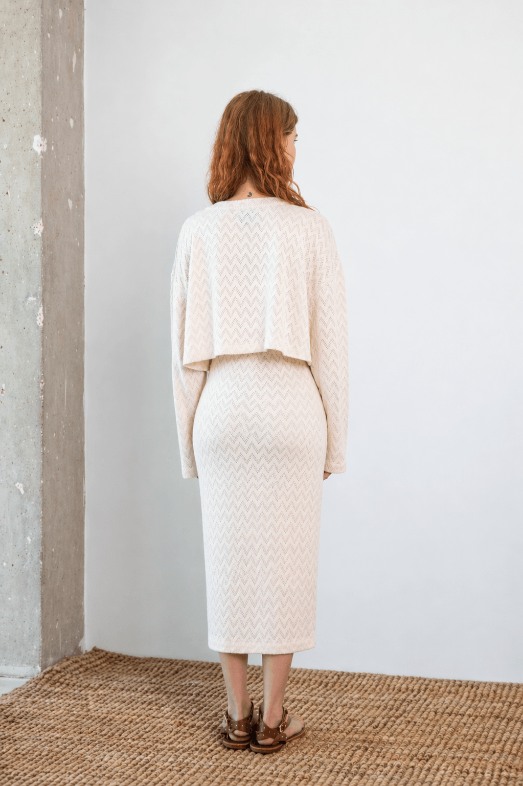Rear view of a model wearing a Crochet Organic Cotton Long Sleeve Top with a cropped silhouette in ecru.