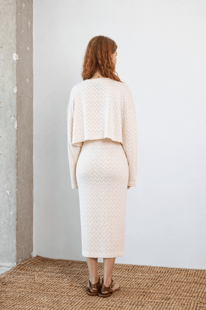 Rear view of a model wearing a Crochet Organic Cotton Long Sleeve Top with a cropped silhouette in ecru.