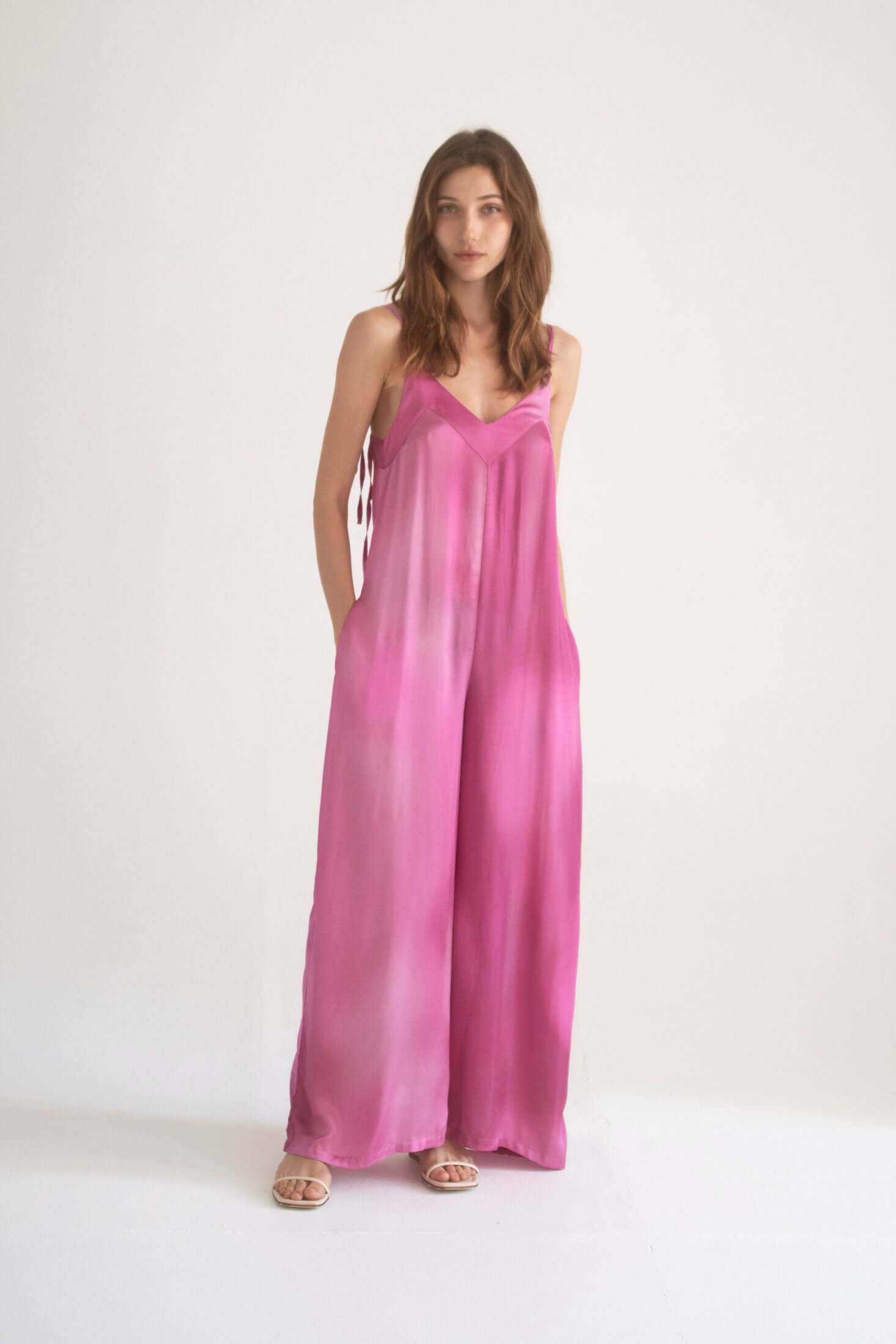 Model wearing a Printed Wide Jumpsuit in pink with adjustable straps and side pockets.
