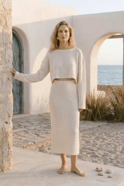 Model wearing a Crochet Organic Cotton Long Sleeve Top with matching skirt, set against a beachside backdrop.